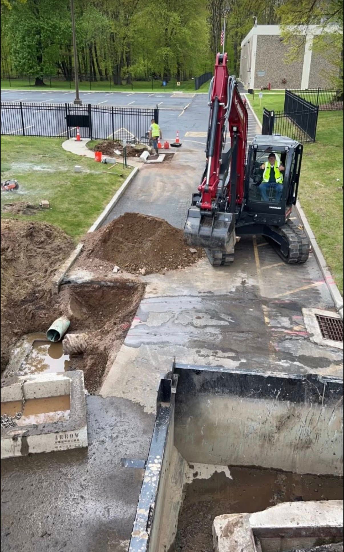 Three gray utility pipes lying in an open trench in an asphalt lot next to a large building.