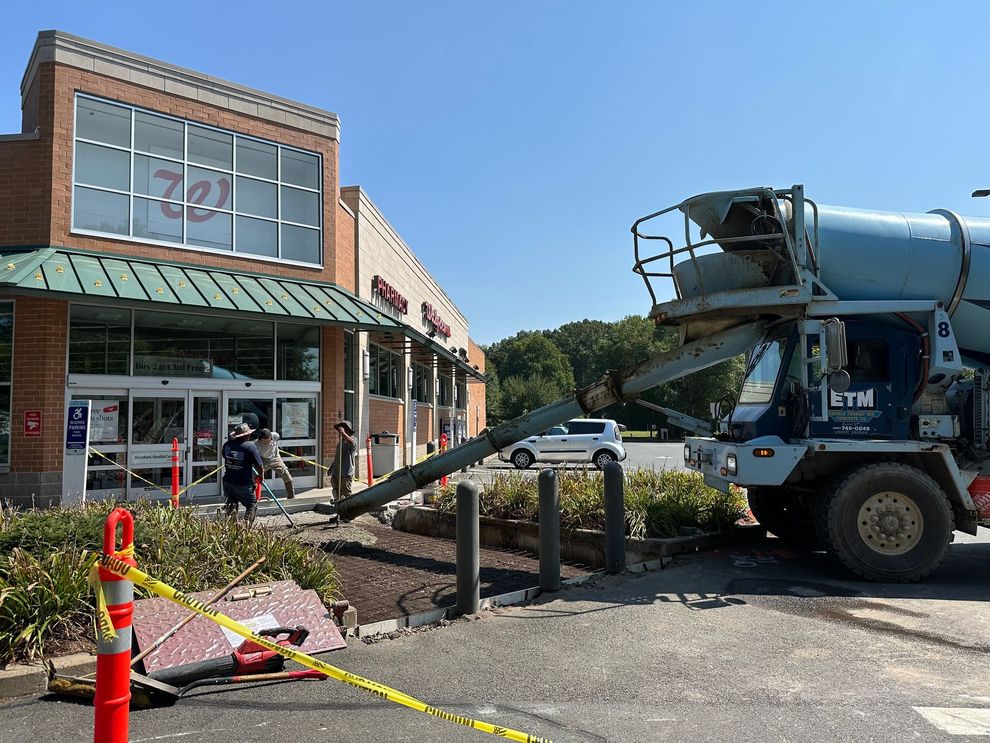 A construction crew in high-visibility gear repaves a parking lot with a road roller and shovels on a sunny day.