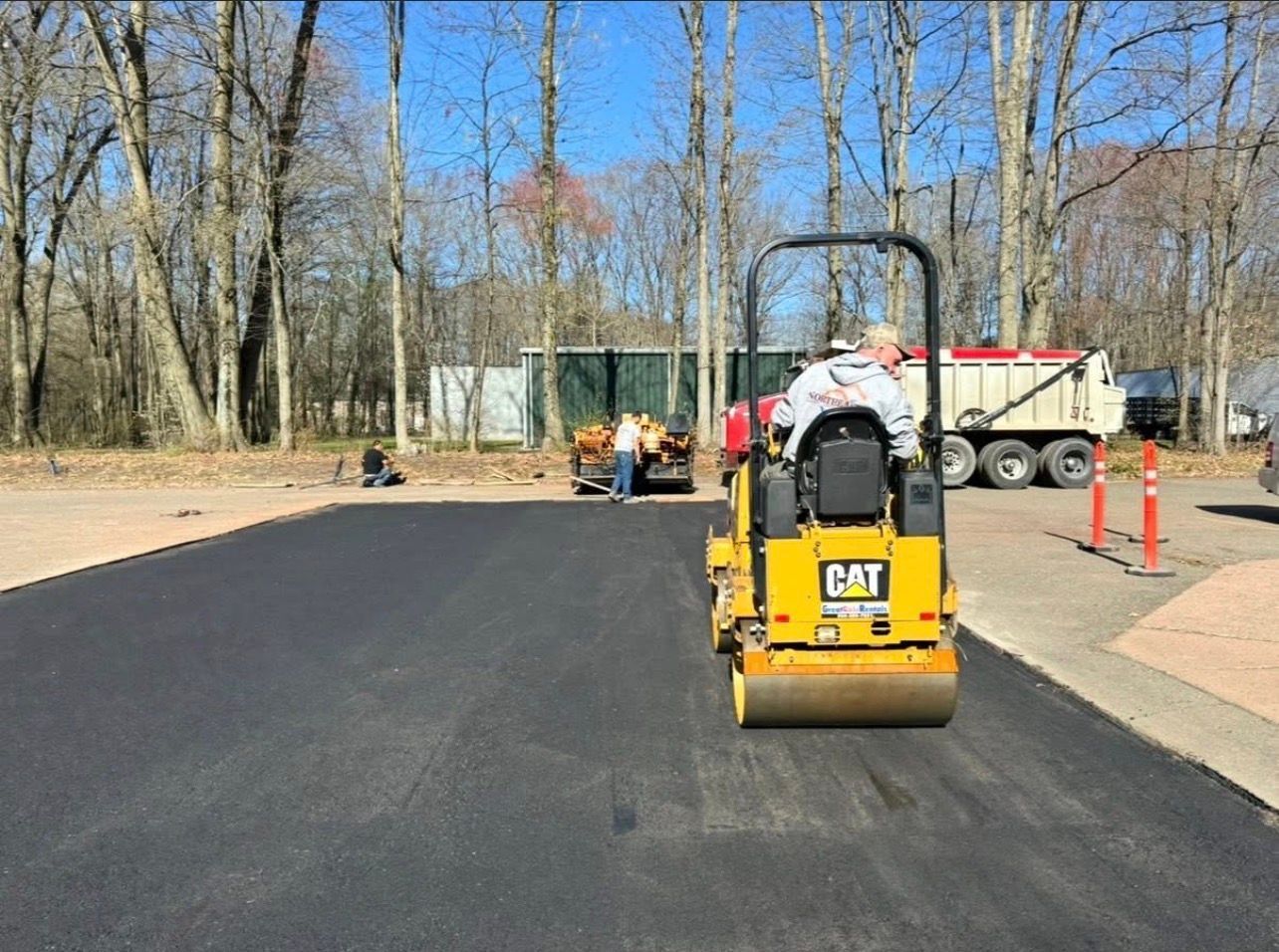 Two workers using tools at a construction site with a textured concrete patio and a stone retaining wall.