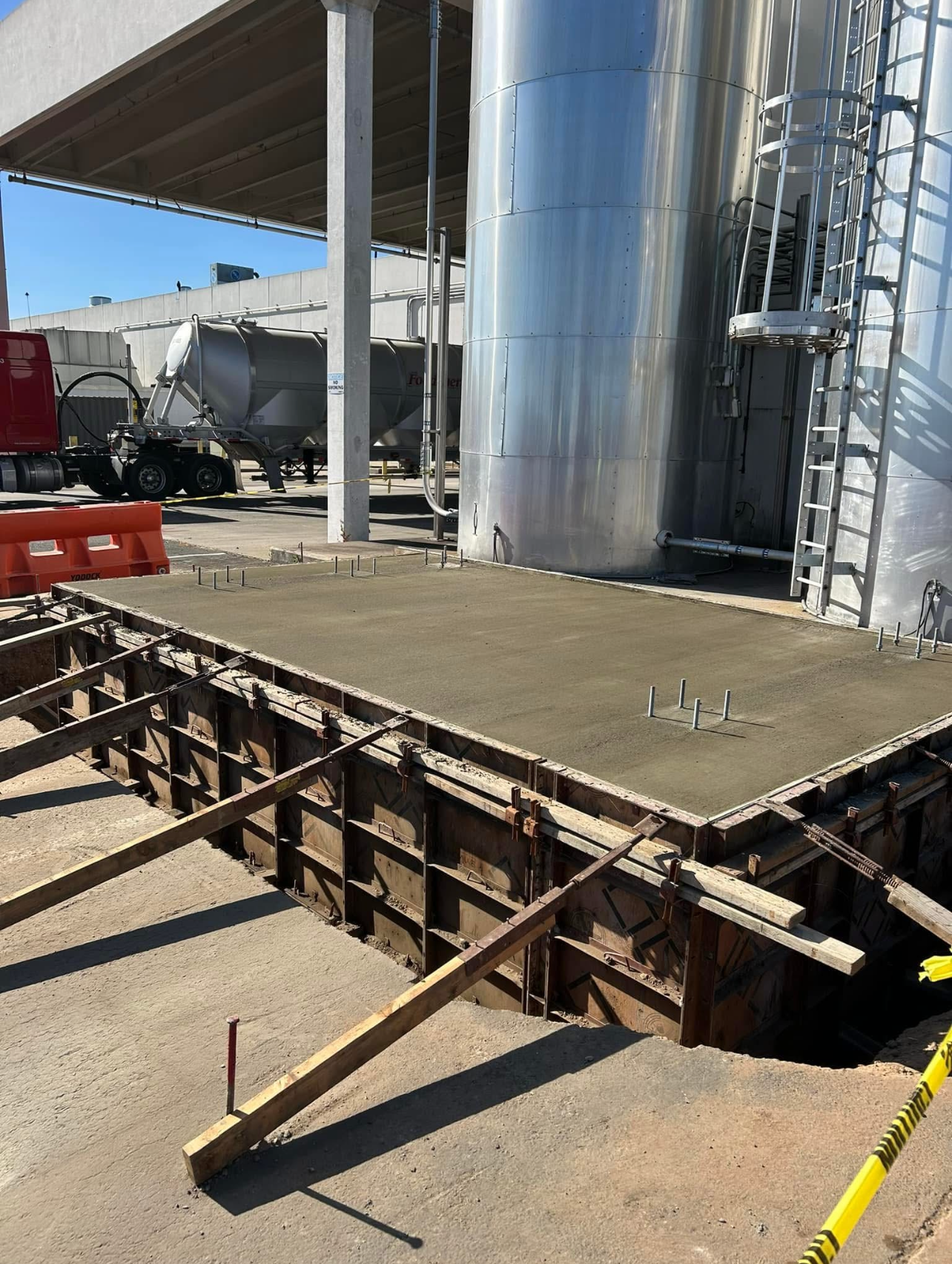 A yellow CAT roller compacts fresh black asphalt on a paved surface with construction vehicles in the background.