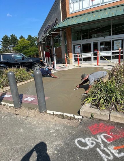 Two people in orange T-Rex costumes stand beside a white dump truck parked on a gravel lot under a clear blue sky.