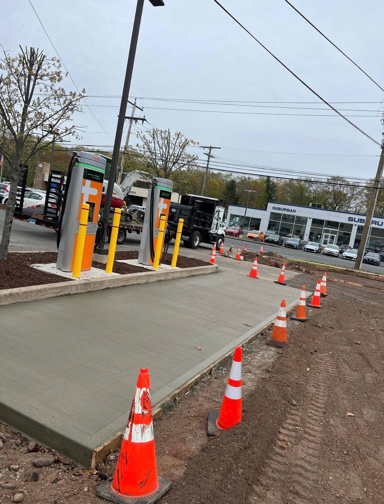 Construction workers in hard hats and safety vests smooth wet concrete on a sidewalk outside a building.