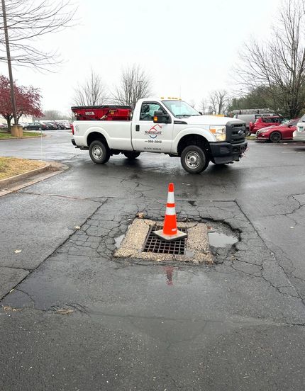 Two workers in high-visibility safety vests and gear digging a rectangular trench in a concrete floor indoors.