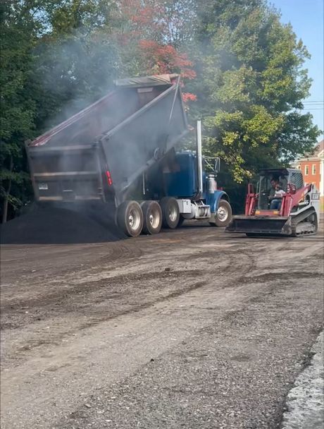 Two people repairing a parking lot patch with a hand tamper and a yellow plate compactor on a sunny day.