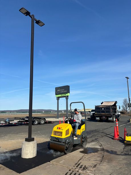 A dump truck and trailer parked on an asphalt lot with some pavement wear and light scattering near a building.