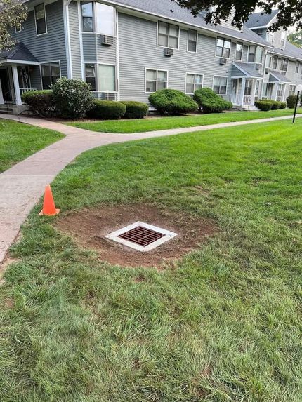 Three workers in high-visibility vests and hard hats pave a parking lot with a piece of heavy construction machinery.