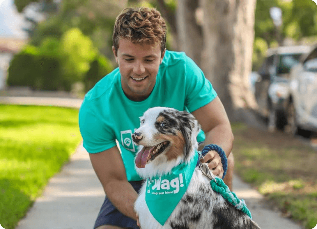 Man petting a dog on a sidewalk. The dog wears a teal bandana and leash. Both are smiling.