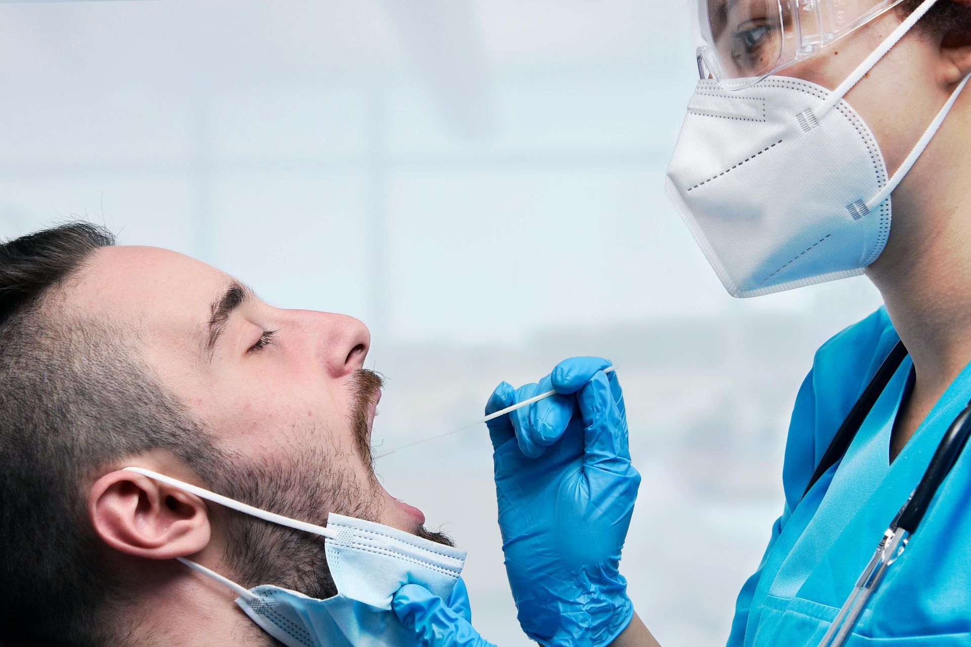 Person getting a PCR test in a medical setting. A healthcare worker in PPE collects a sample with a swab.
