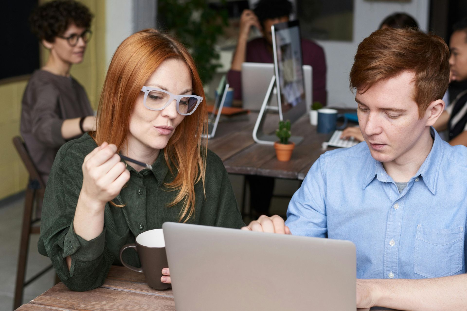 Woman in glasses and man with red hair looking at a laptop in an office setting.
