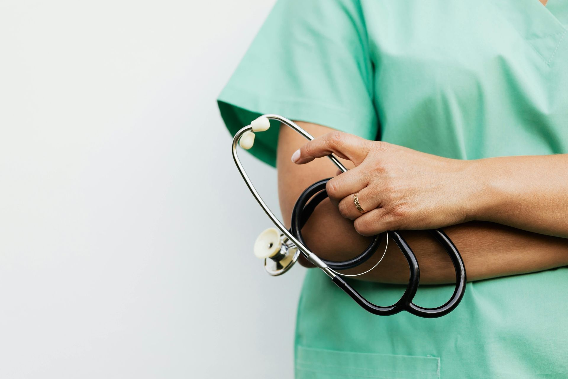 Nurse in green scrubs holding a stethoscope against a white background.