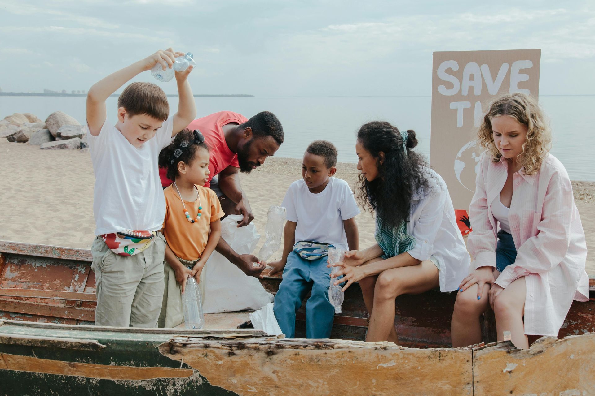 Volunteers cleaning up plastic on a beach, sitting in a boat. Cardboard sign reads