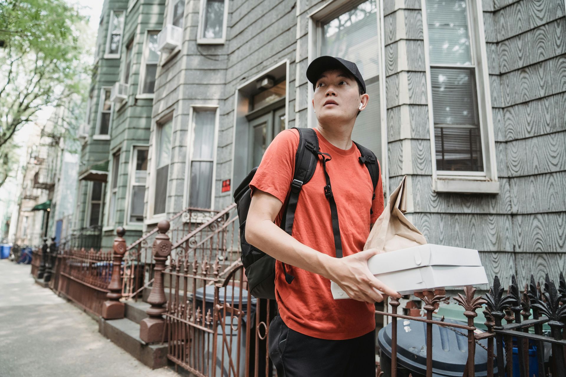 Delivery person holding food packages, walking towards apartment building.