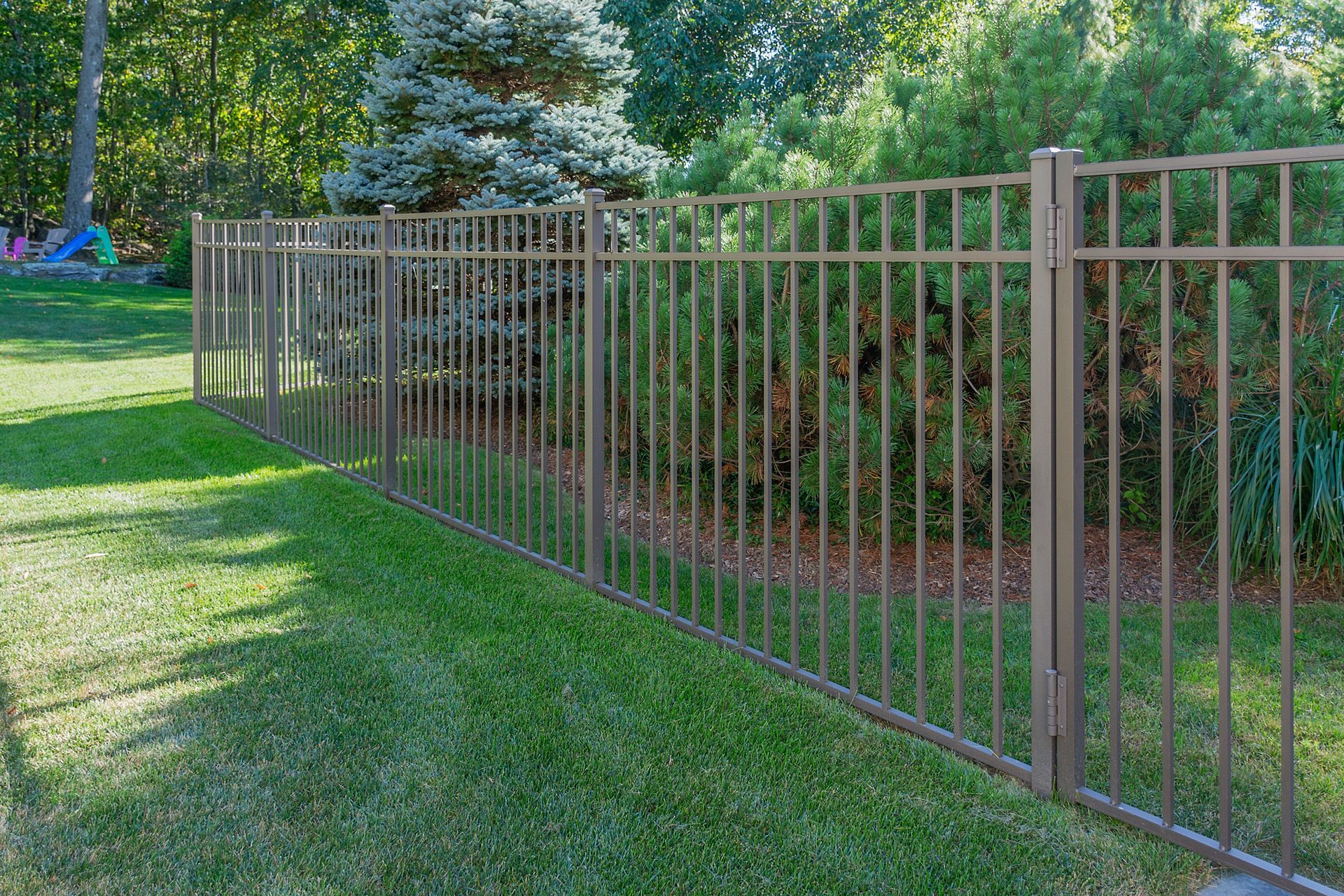 A metal fence surrounds a lush green lawn in a backyard.