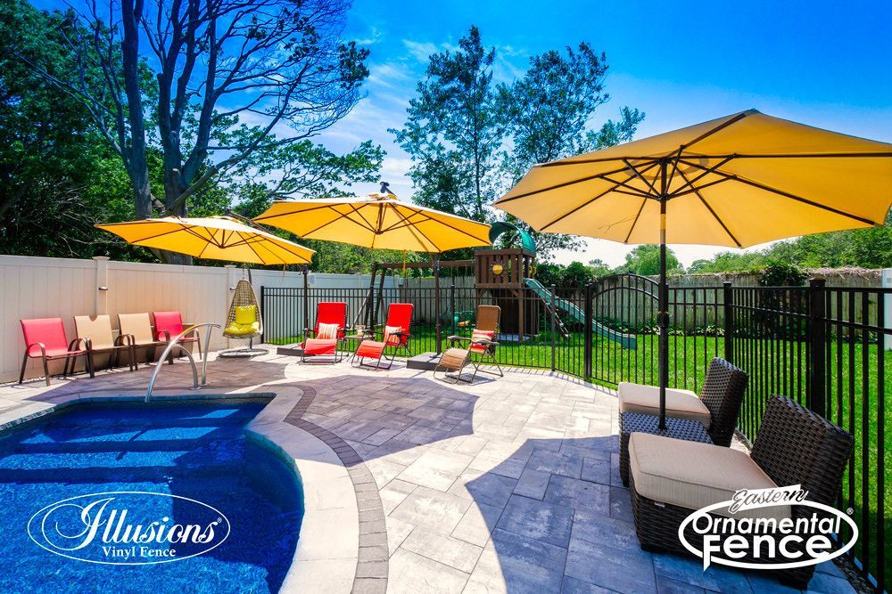 A backyard with a pool , chairs , umbrellas and a fence.
