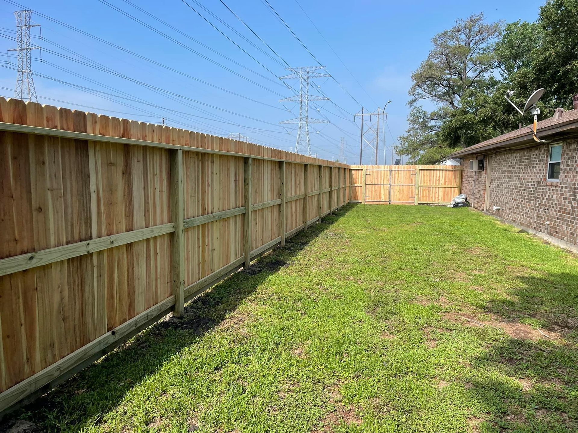A wooden fence surrounds a lush green yard in front of a house.