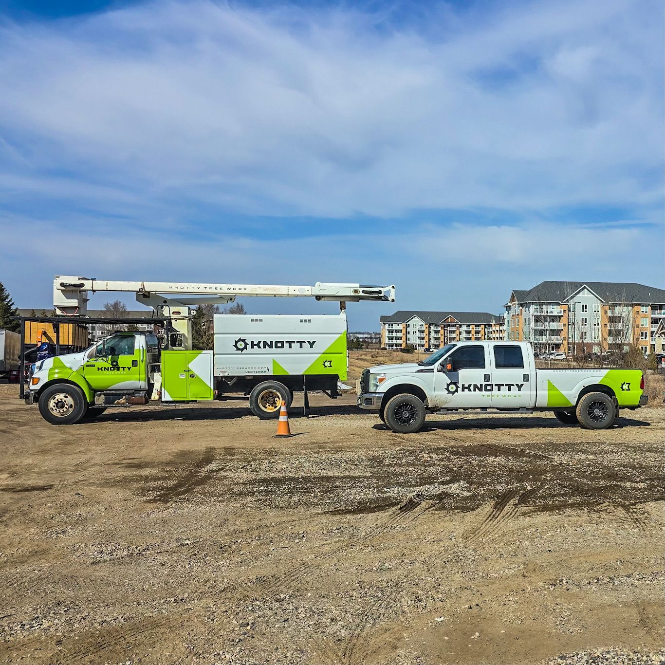 Two utility trucks with boom lifts parked on a gravel lot under a blue sky.