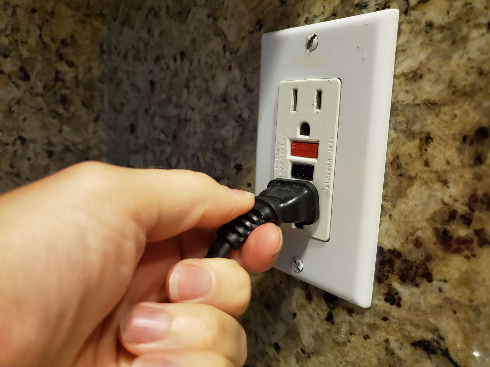 Close-up of a GFCI outlet with test and reset buttons being installed by a residential electrician.