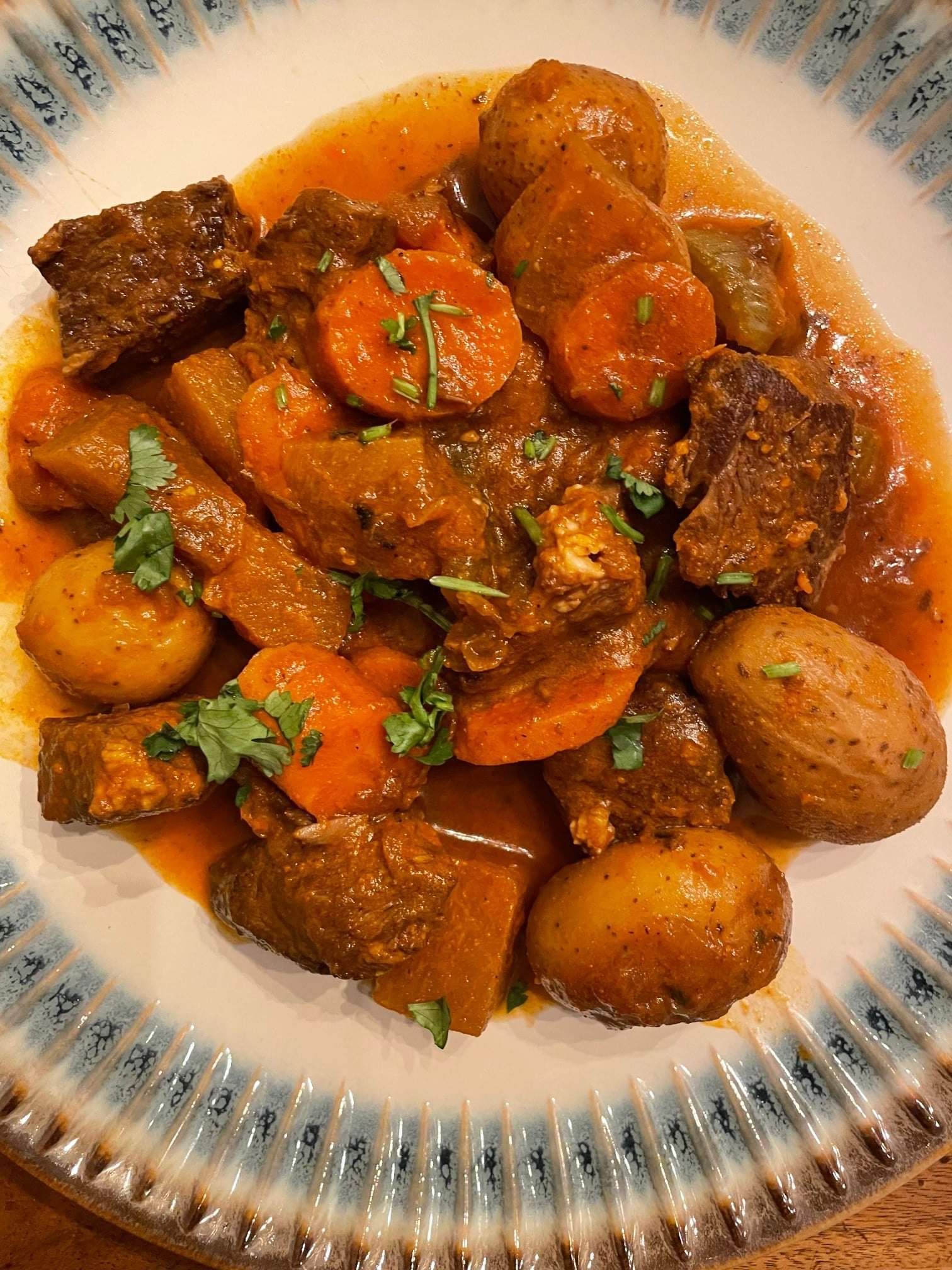 A hearty beef stew with potatoes, carrots, and herbs served in a shallow bowl with a blue and white patterned rim.