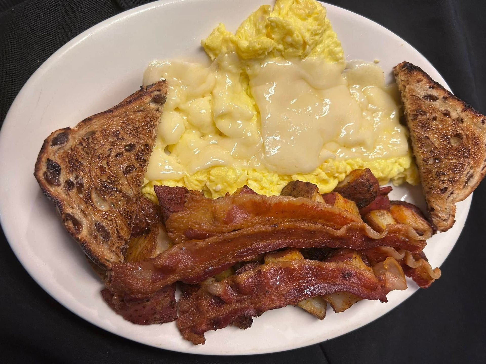 A plate of breakfast food featuring scrambled eggs topped with melted cheese, crispy bacon, and two pieces of toast.
