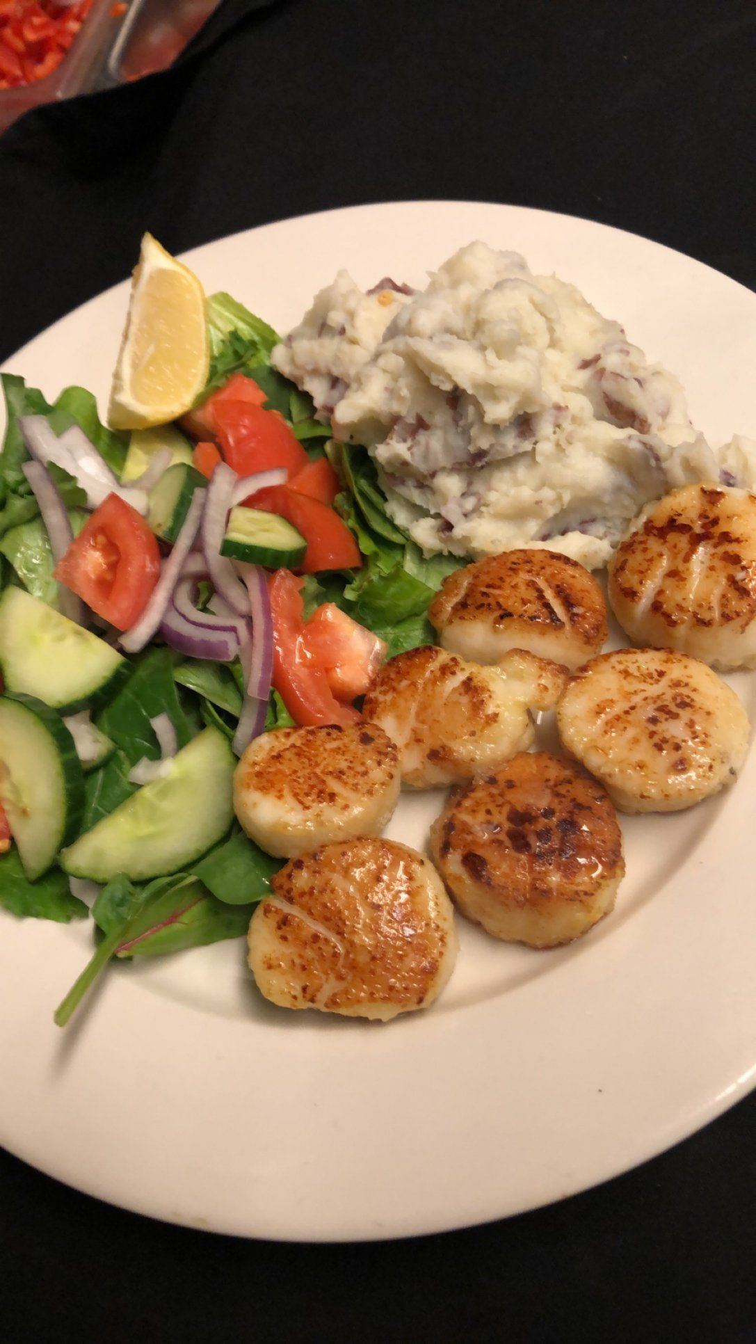 A plate featuring seared scallops, a scoop of mashed potatoes, and a fresh garden salad with a lemon wedge.