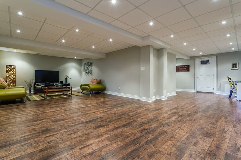 a living room in a basement with hardwood floors and a flat screen tv .