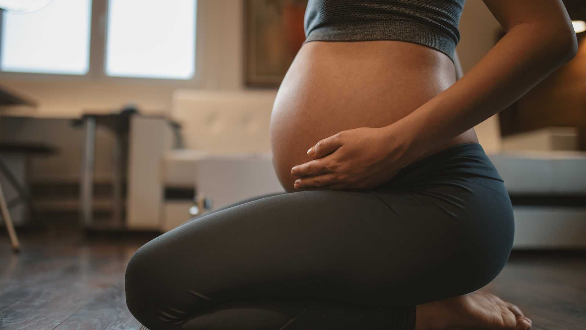 A pregnant woman is kneeling down and holding her belly.