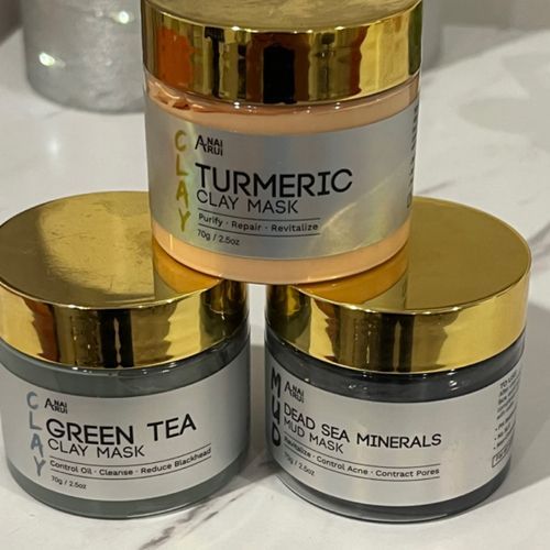 Three jars of turmeric clay mask and green tea clay mask are stacked on top of each other on a counter.
