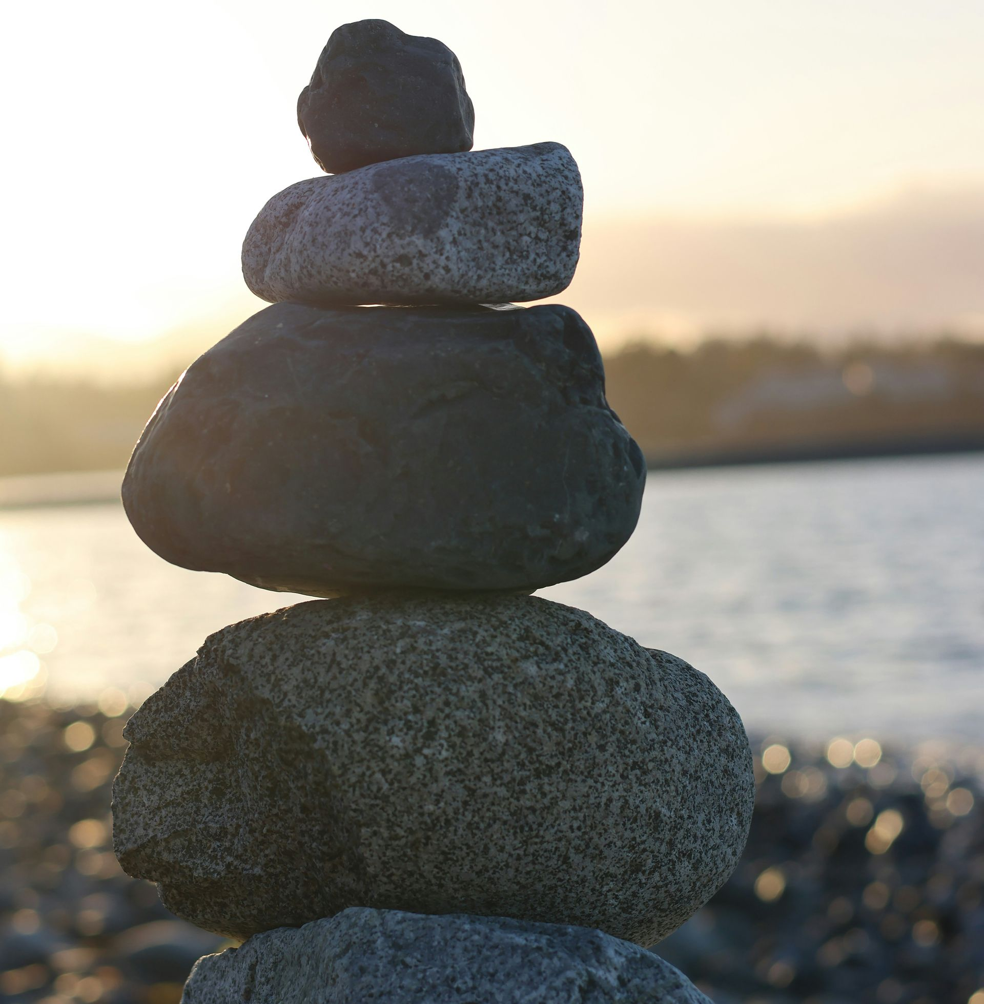 Stack of balanced stones on a beach, with water and a sunset in the background.