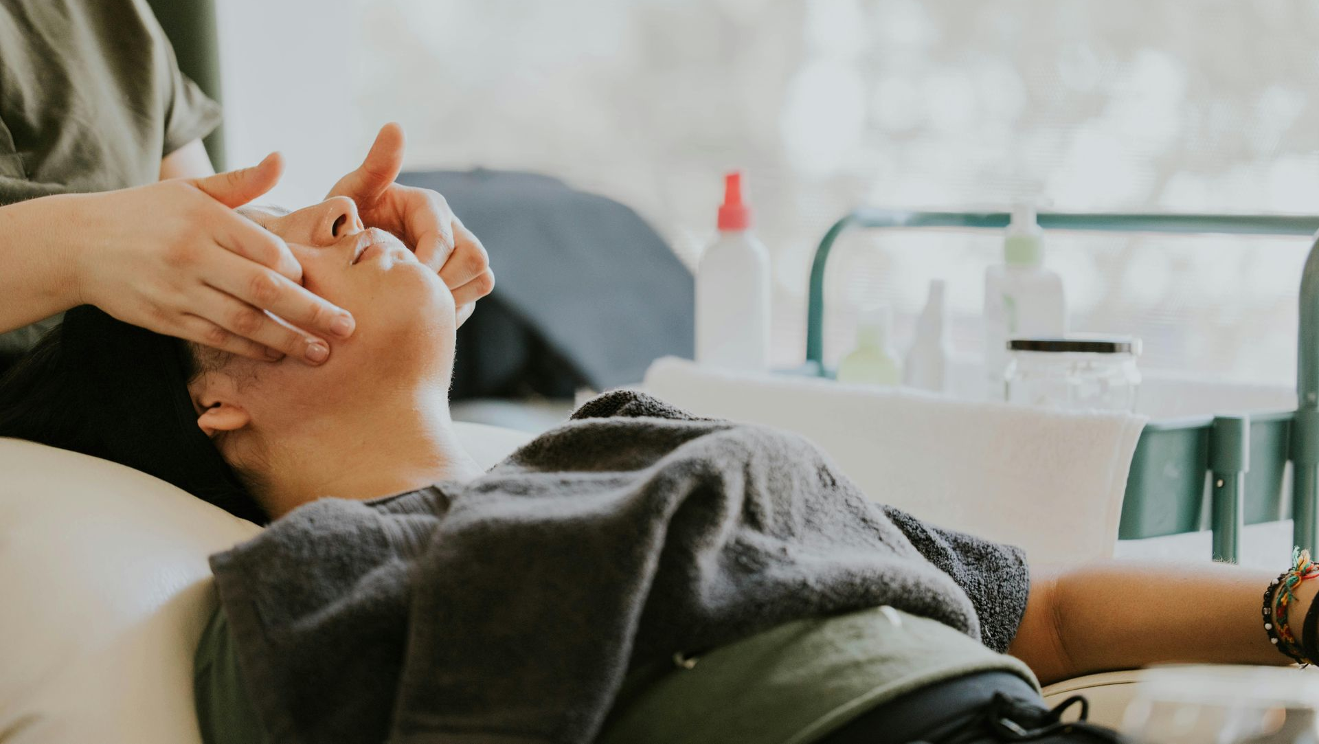 Person receiving facial massage in a spa setting, hands on face, eyes closed.