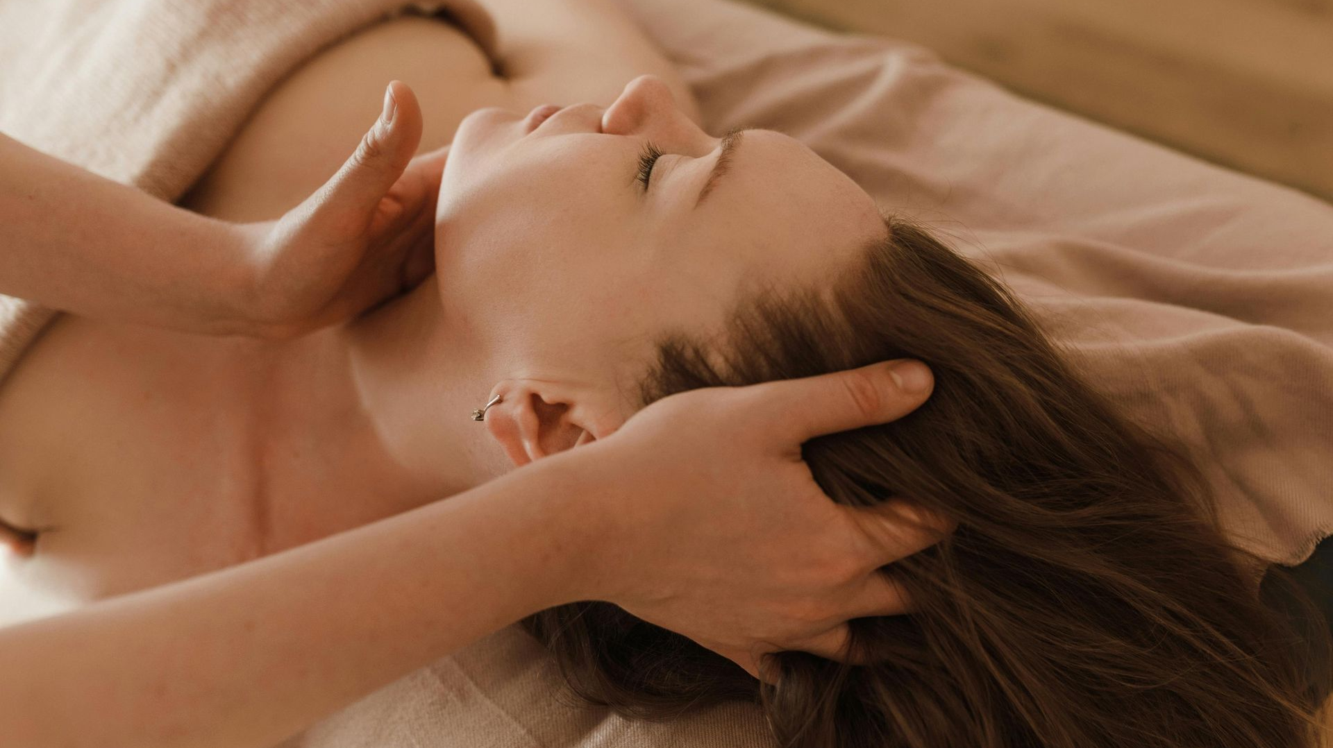 Woman receiving a head massage on a massage table, in a spa setting.