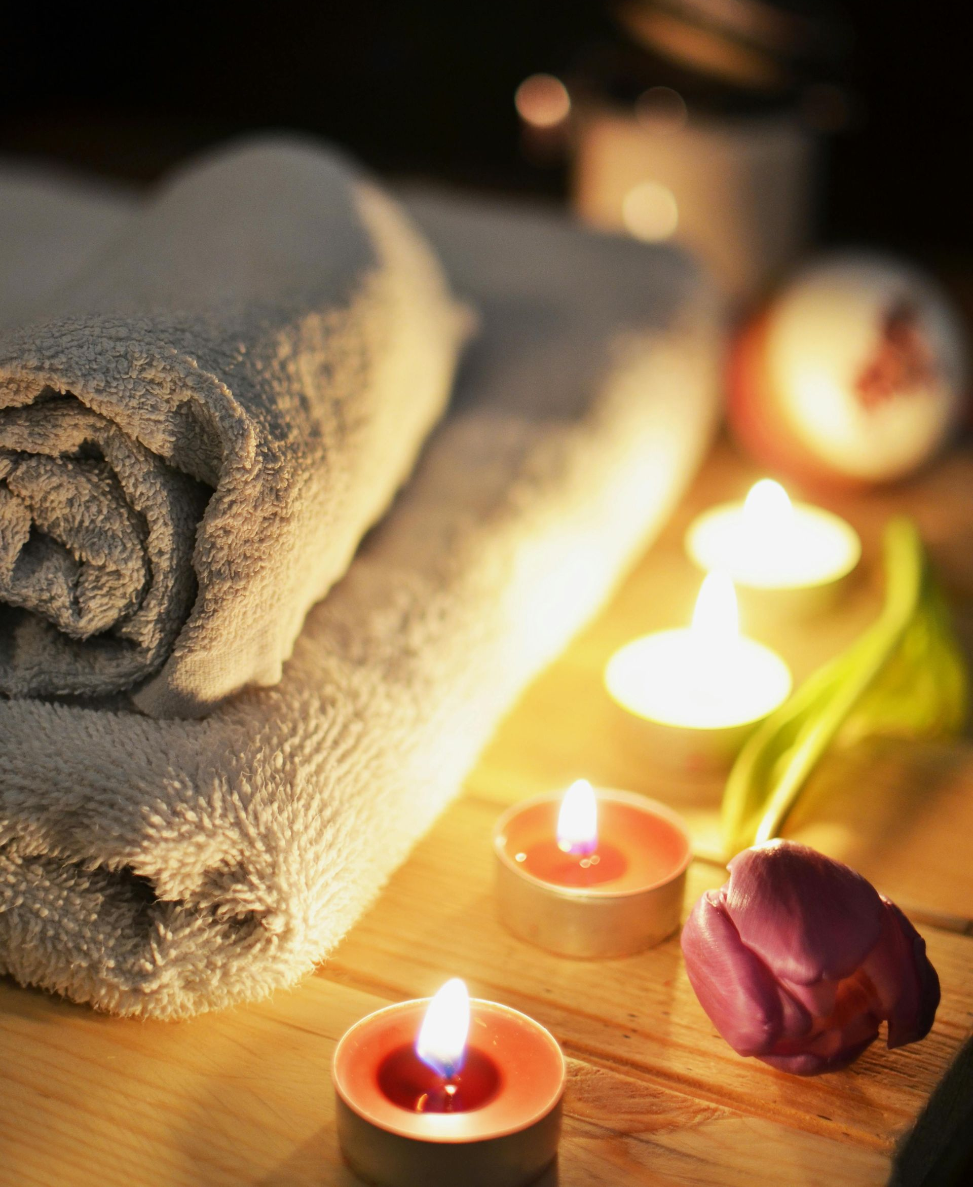 Rolled towels, lit candles, and a purple tulip for spa relaxation.