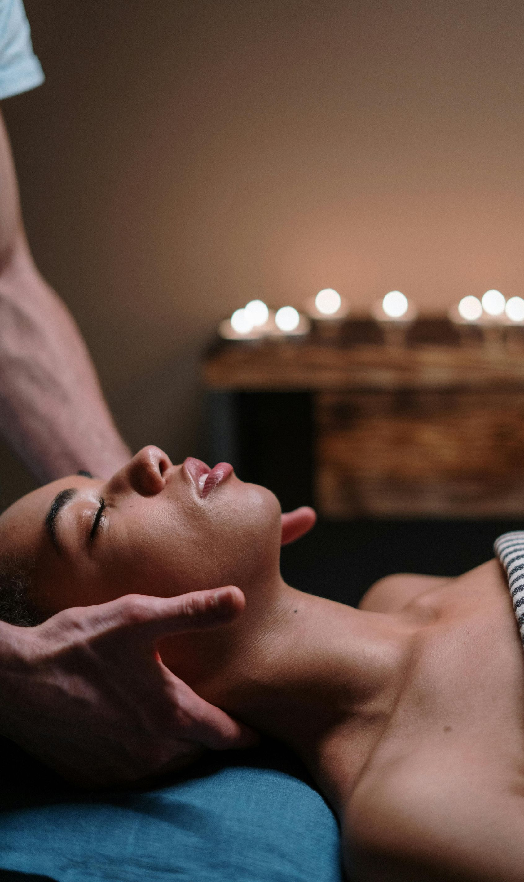 Person receiving a neck massage in a dimly lit room; candles in the background.