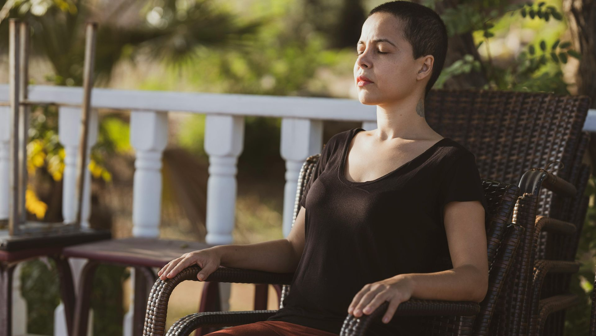 Woman with short hair seated, eyes closed, outdoors on a sunny day.