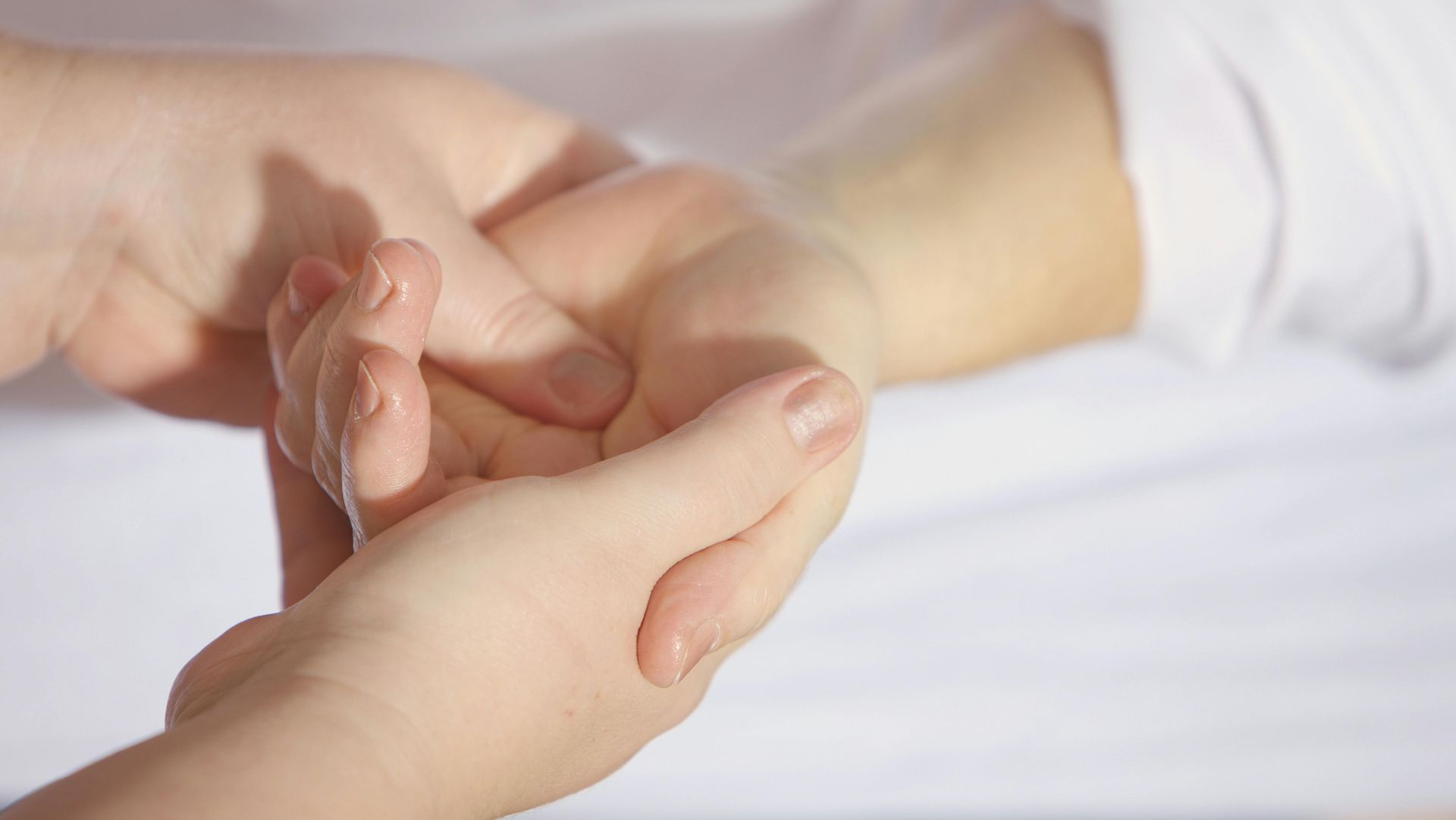 Hands gently massaging another person's wrist and palm. White sheets in the background.