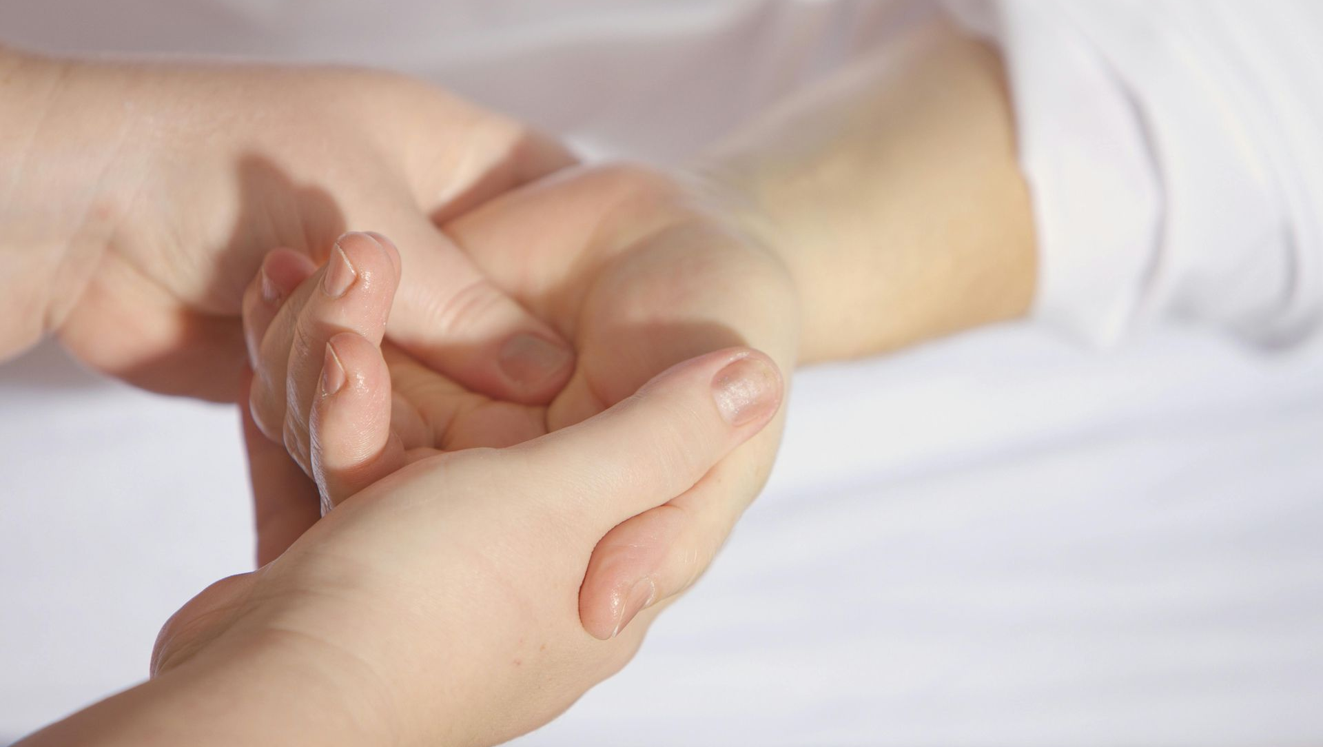 Hands of one person gently holding another’s wrist. White background.