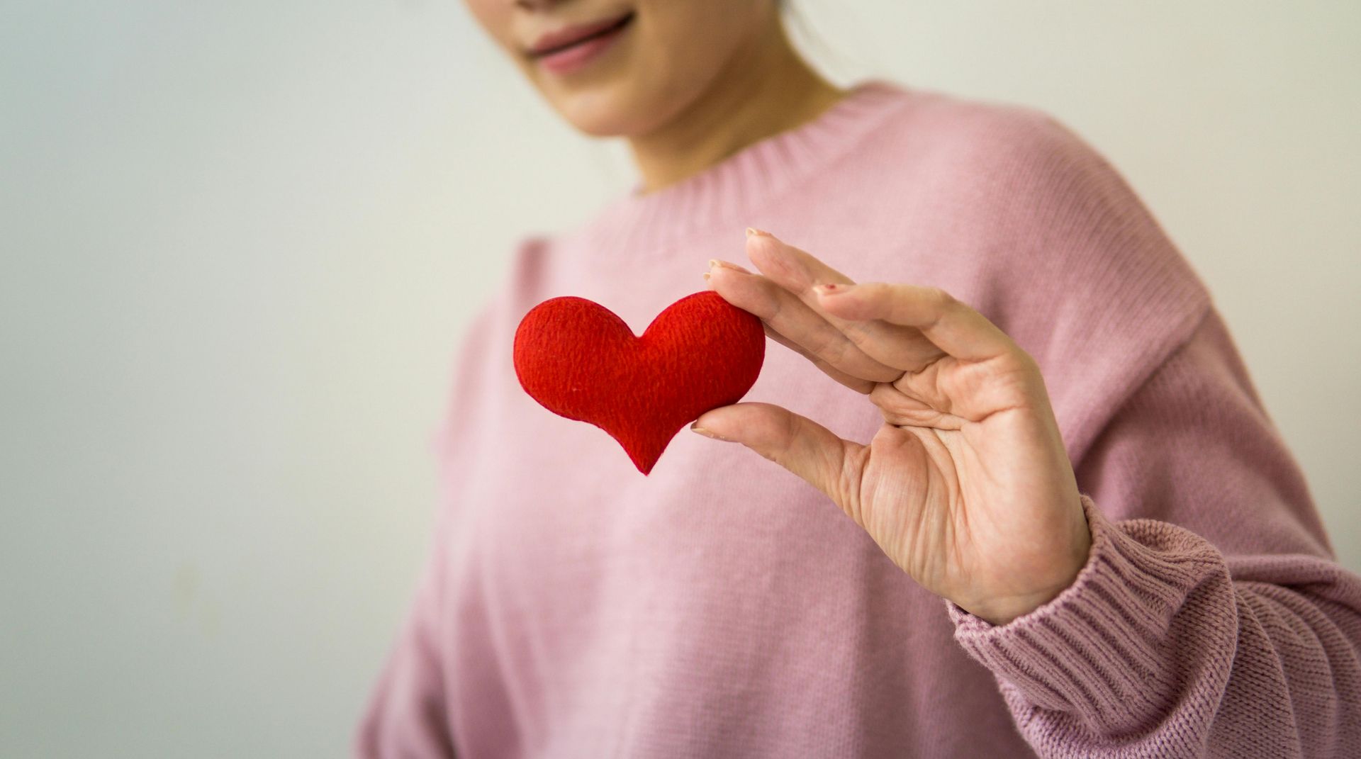 Woman in pink sweater holds up a small, red heart.