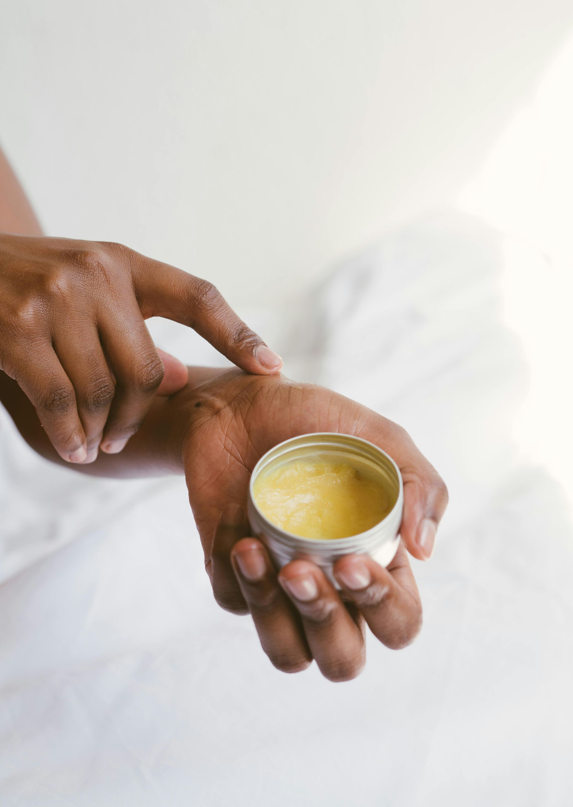 Person applying balm from a small tin to their wrist.