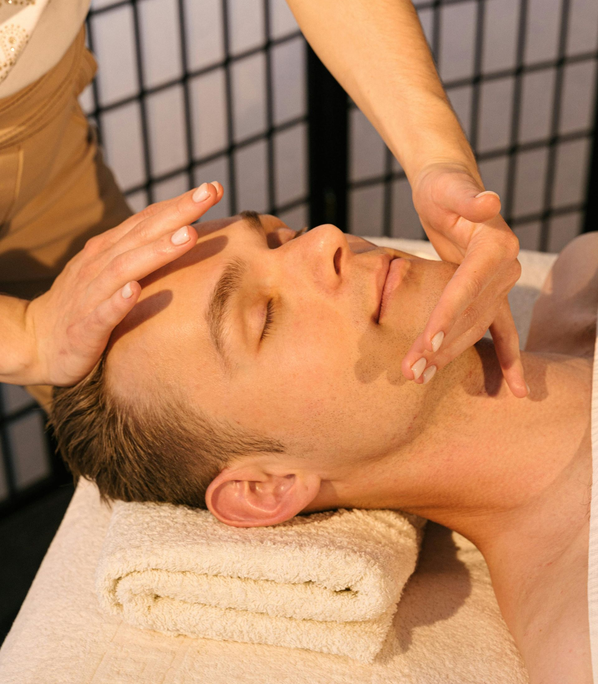 Man receiving facial massage, lying on a massage table with hands on his face.