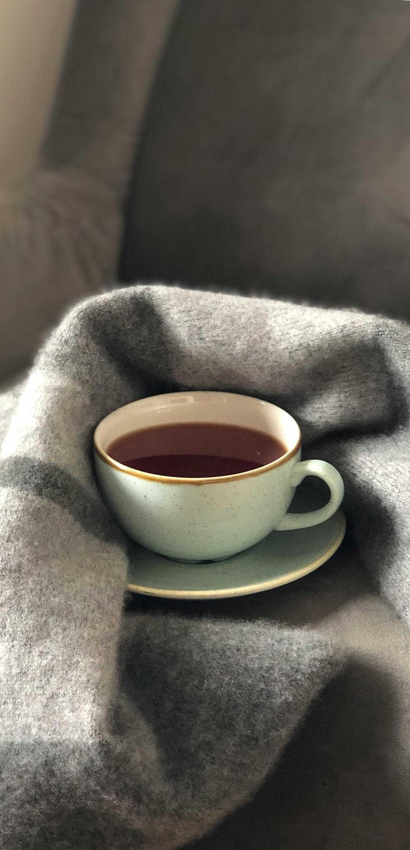 Blue teacup on saucer, filled with tea, on a gray blanket.