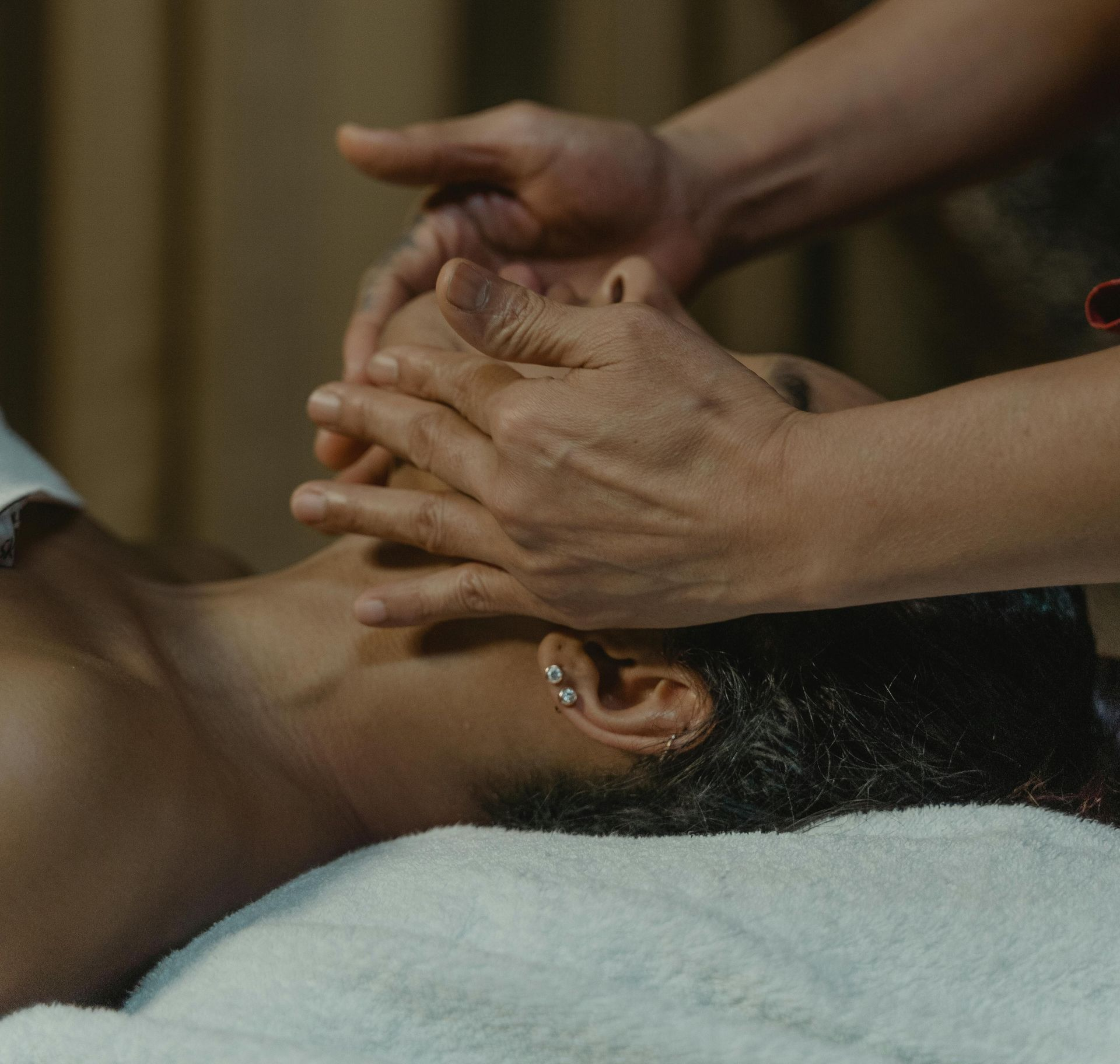 Hands massaging a person's face. The person lies on a towel, receiving facial treatment.