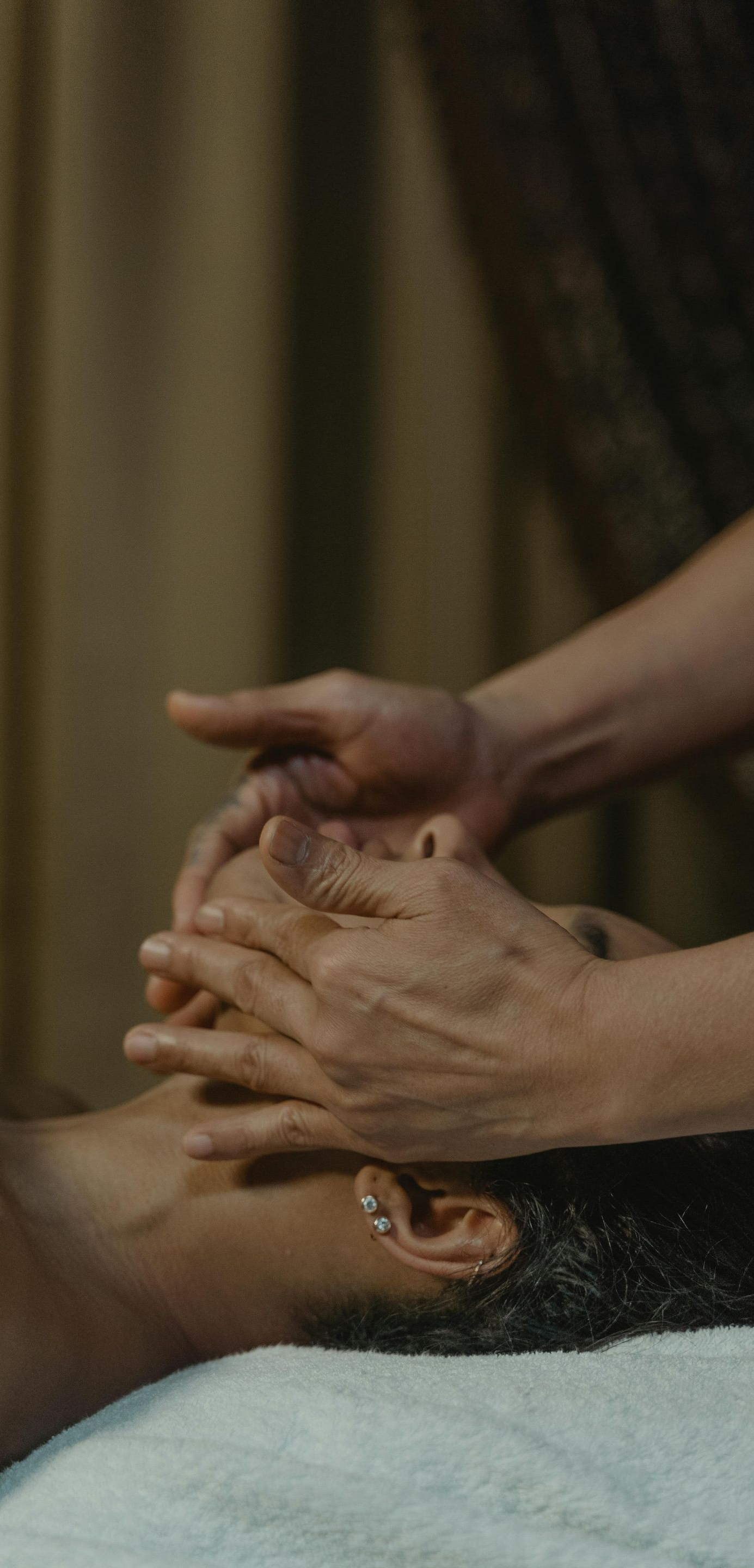 Hands performing facial massage on a person lying down on a massage table.