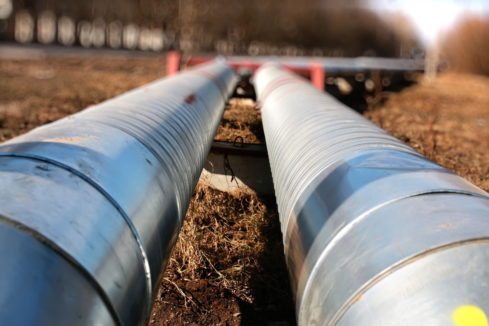 Two large metal pipes laid parallel on the ground outdoors, supported by red brackets over soil.
