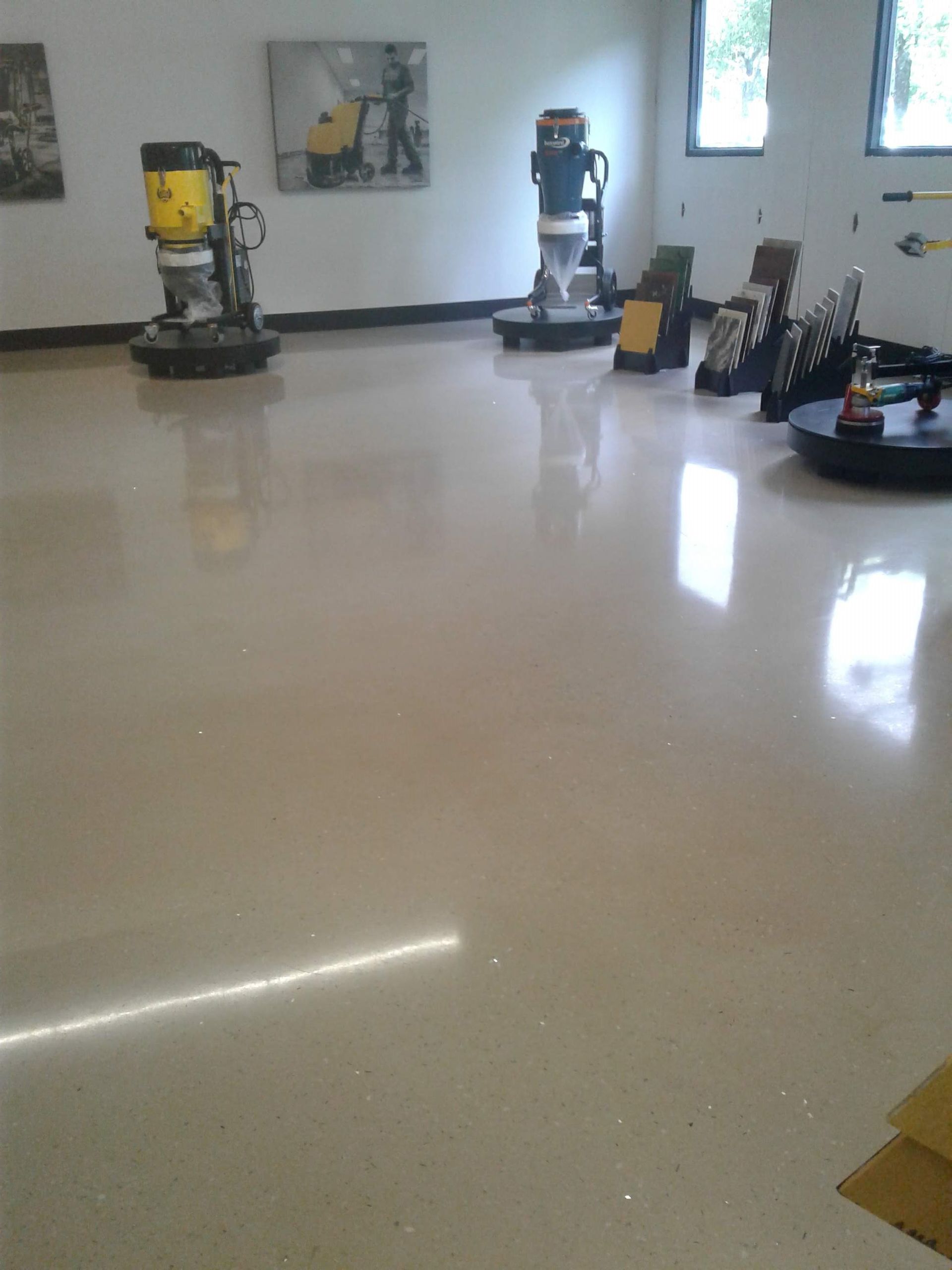 Shiny concrete floor with grinding machines in an empty room. Sunlight reflects.