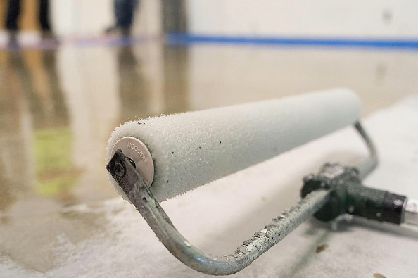 Paint roller laying on wet, light-colored flooring; someone is in the background, painting.