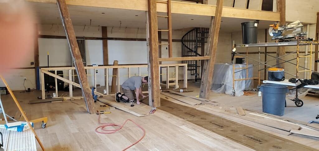 A man is working on a wooden floor in a large room