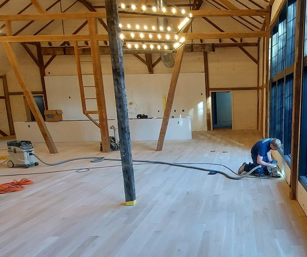 A man is working on a wooden floor in a large room