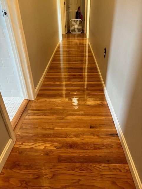 A hallway with hardwood floors and a fan on the wall.