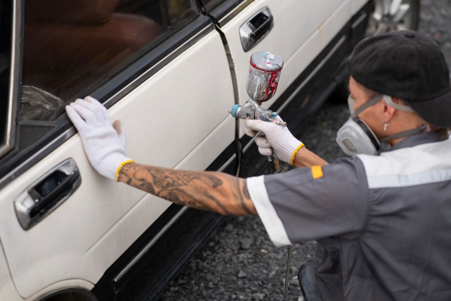 Person painting a car door, wearing protective gear, with tattoos visible on their arm.