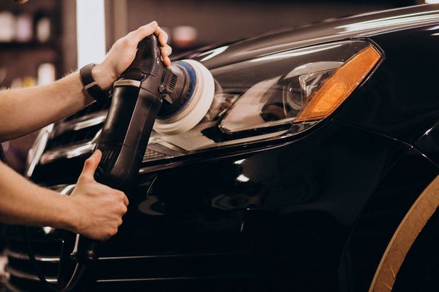 Person polishing a black car headlight with a machine.