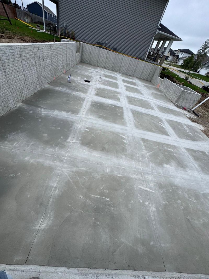Newly poured concrete patio surface with a grid of control joints, set between two gray concrete retaining walls.